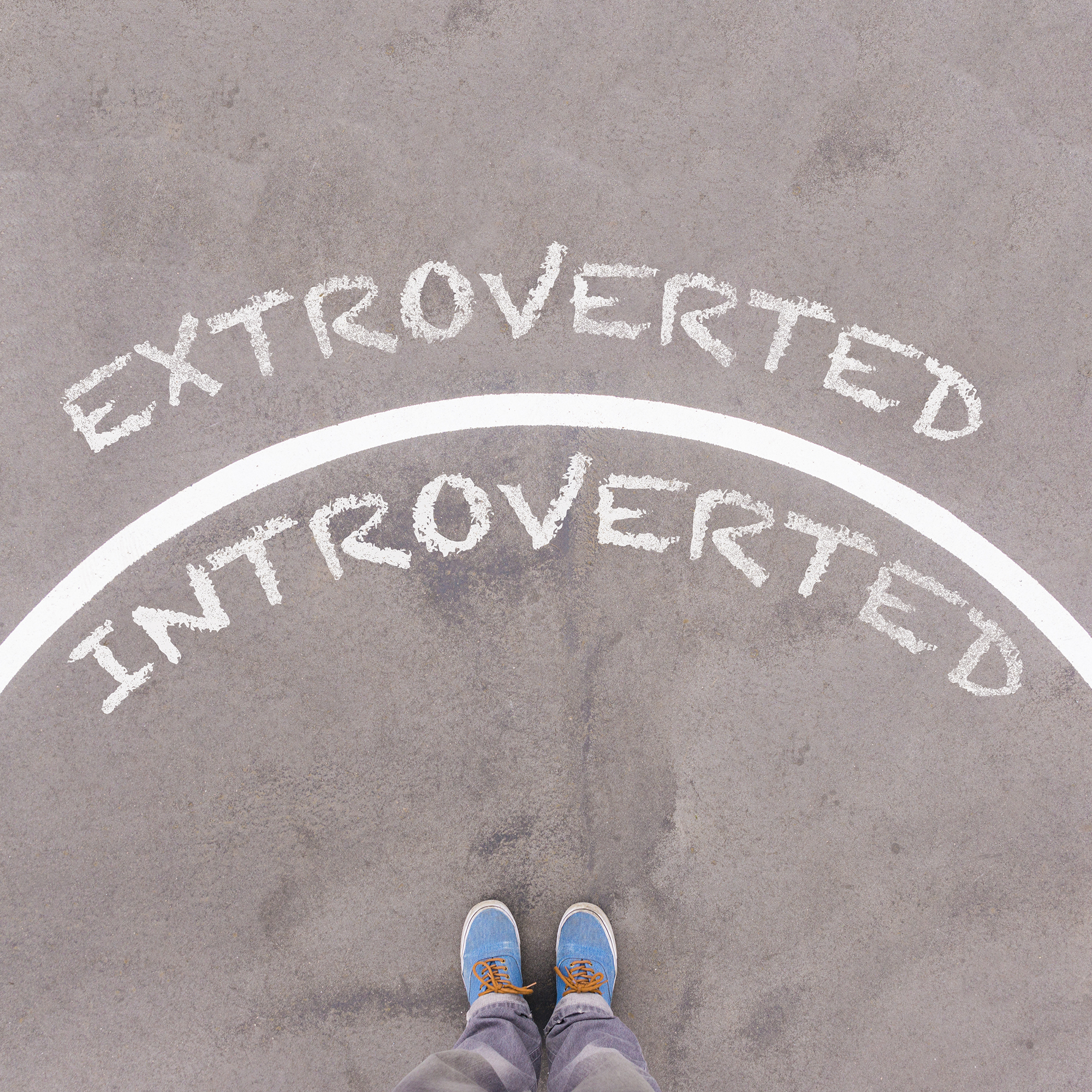 Extroverted vs Introverted text on asphalt ground, feet and shoes on floor, personal perspective footsie concept